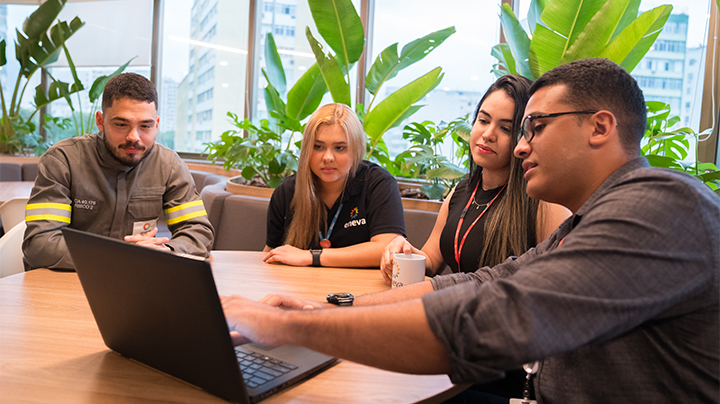 Grupo de estagiário da Eneva conversando. Na foto é possível olhar duas mulheres e dois homens. Um deles aponta para o computador enquanto os demais observam.
